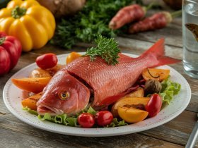 Peixe vermelho assado em cama de legumes com um betta vermelho em aquário ao fundo