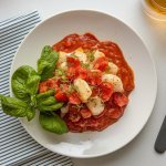 Prato de macarrão com sardinha e molho de tomate, finalizado com salsinha fresca, servido em um prato branco.