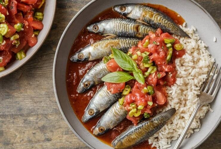 Sardinha na panela de pressão simples e fácil, servida em um prato com molho de tomate e salsinha, acompanhada de arroz branco.